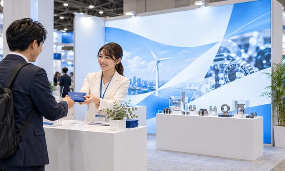商品展示が見えるブースで来場者にノベルティを手渡すスタッフ｜誉展示会
